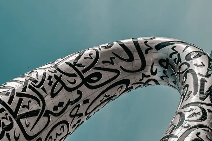 A curve of the Museum of the Future's steel shell carries Arabic calligraphy against a clear sky.