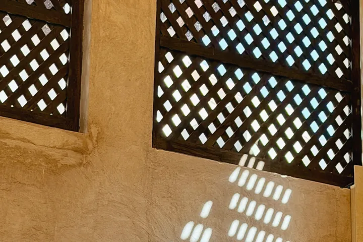 Sunlight through two lattice windows lays a pattern of light across a plaster wall.